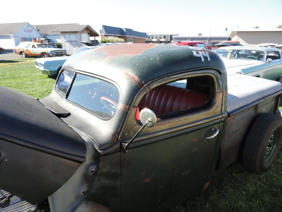 Old dark green pickup truck with red interior and a number 44 on the roof. Other cars are parked in the background