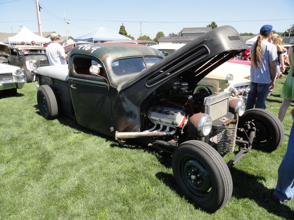 Rat rod pickup truck with hood open, showing V8 engine. Number 1964 is painted on the roof