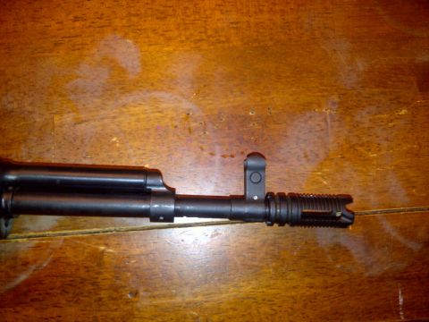 1989 Ford Bronco - Close-up of a firearm barrel, showing the front sight and muzzle device against a wooden background.