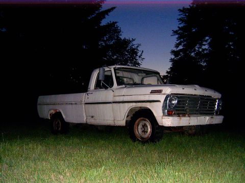 1967 Ford F-250 - A white 1967 Ford F-250 pickup truck sits in a grassy area with trees in the background as the sky darkens.