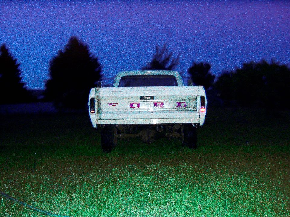 Rear view of a white Ford pickup truck at dusk. The tailgate has 'FORD' spelled out in block letters