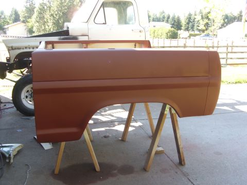 1967 Ford F-250 - A brown truck bed side panel, likely from a 1967 Ford F-250, is displayed on sawhorses in front of a white truck cab.