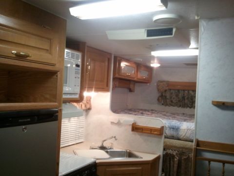 1967 Ford Mustang - The interior of a camper features a kitchen area with a microwave and sink, adjacent to a sleeping area.