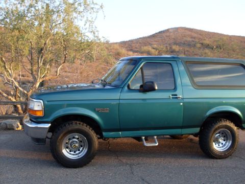 1996 Ford Bronco - Side view of a green 1996 Ford Bronco parked on a paved surface with arid vegetation.