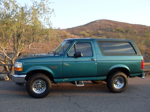1996 Ford Bronco - A side view of a green 1996 Ford Bronco parked outdoors with a desert-like landscape behind it.