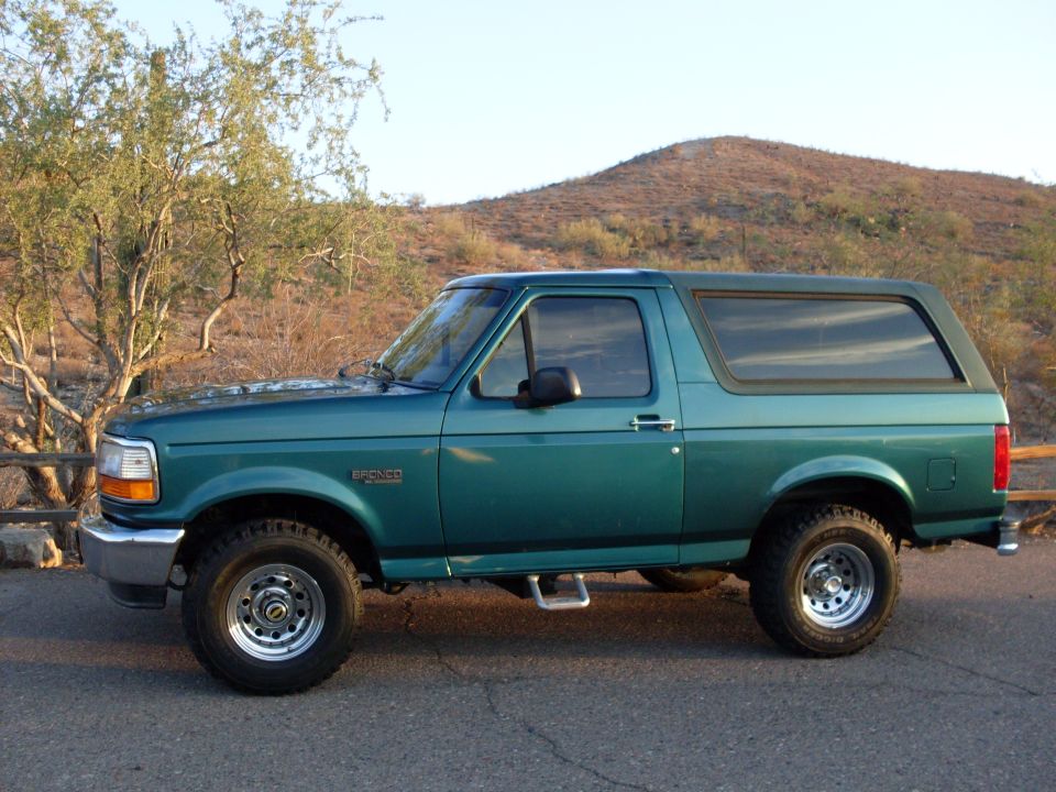 Green 1996 Ford Bronco parked on a road with a hill and trees in the background