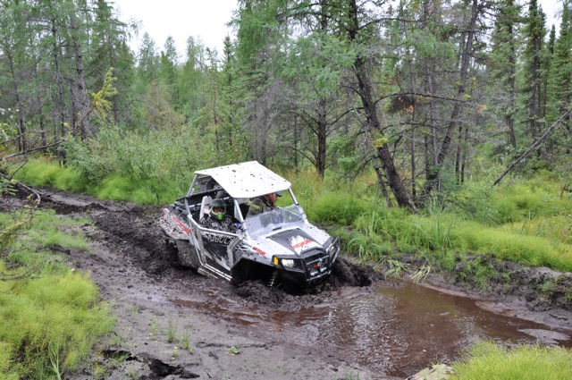 White and black side-by-side off-road vehicle stuck in mud on a wooded trail