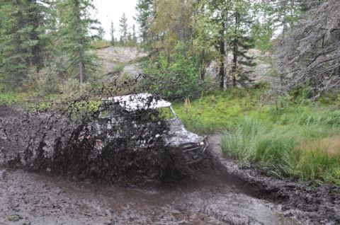 1986 Ford F-150 - An off-road vehicle powers through a muddy trail, kicking up a large spray.