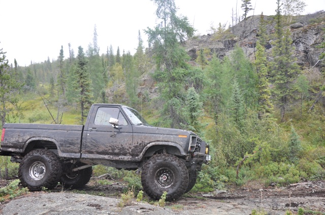 Muddy lifted pickup truck with large tires driving on a rocky trail in a wooded area