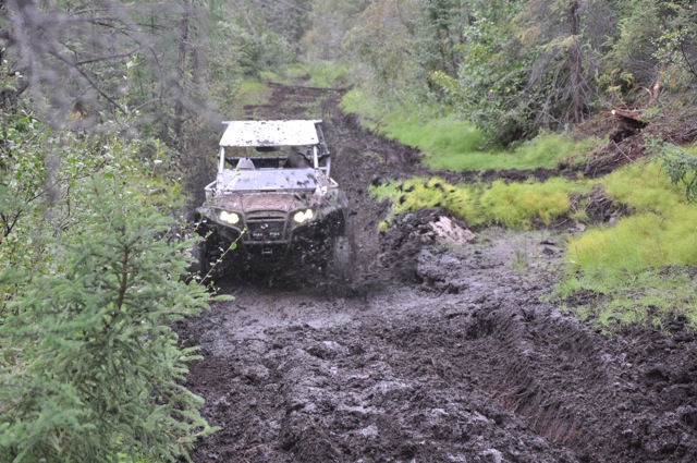 Side-by-side off-road vehicle splashing through mud on a forest trail