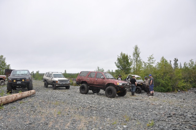 Several off-road vehicles parked on a gravel lot with trees in the background