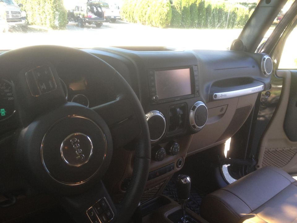 Interior shot of a Jeep Wrangler, showing the steering wheel, dashboard, and center console. The Jeep logo is visible on the steering wheel