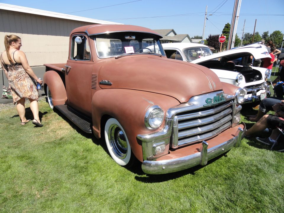 Brown 1950 GMC pickup truck with chrome grille and wide whitewall tires parked on grass