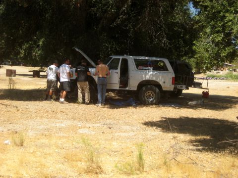 1996 Ford Bronco - A group of men work on a white Ford Bronco parked under trees in a dry, outdoor setting.