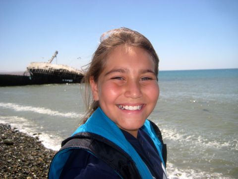 1996 Ford Bronco - A shipwreck rests on the shore under a clear blue sky, with a young person smiling at the camera.