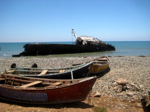 1996 Ford Bronco - A large shipwreck rests partially submerged on a pebble beach, with several small rowboats pulled ashore.