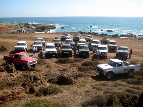 1996 Ford Bronco - A large group of off-road vehicles assembled near the coast on a sunny day.