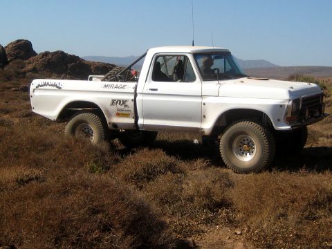 1996 Ford Bronco - This white pickup truck, modified for off-road use, is seen in a desert environment.