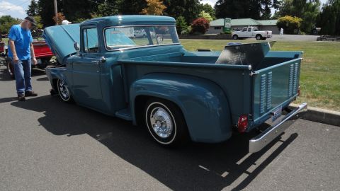 1964 Ford Fairlane - A blue pickup truck is parked with its hood up, while a man stands next to it. Another white truck is visible in the background.