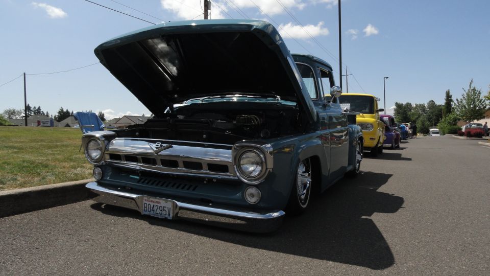 Blue 1956 Ford F-100 pickup truck with hood open, parked on street