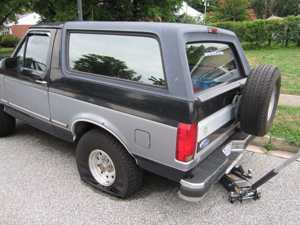 Ford Bronco with flat tire on rear passenger side, jack under bumper