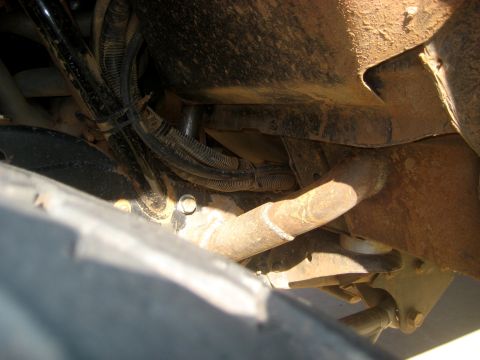 1996 Ford Bronco - The underside of a vehicle shows various mechanical parts and wiring harnesses covered in dirt and grime.