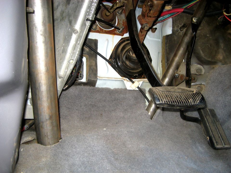 Vehicle interior showing pedals, floor mat, and roll cage tubing