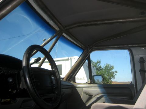 1996 Ford Bronco - The interior of a vehicle is visible, a custom roll cage structure and a view through the windshield and side window.