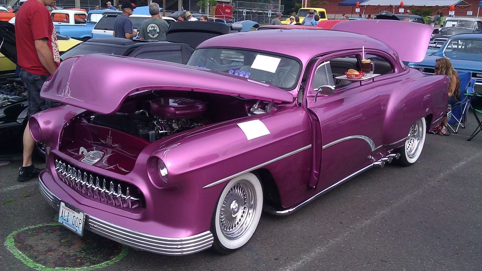 Purple hot rod with hood and trunk open, burger and drink on a tray attached to the window