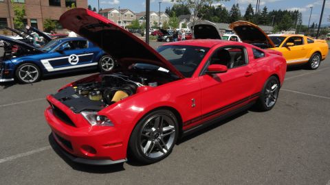 1964 Ford Fairlane - A red Ford Mustang GT500 is parked with its hood open, alongside other Mustangs at a car show.