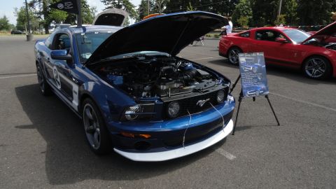 1964 Ford Fairlane - A blue Ford Mustang is displayed with its hood open, alongside a red Mustang and an informational sign.