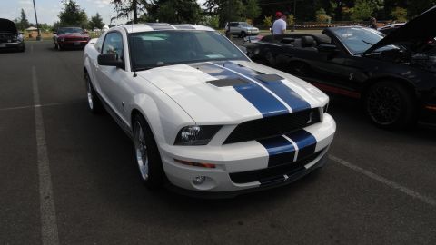 1964 Ford Fairlane - A white Ford Mustang with blue racing stripes is parked next to a black convertible Mustang.