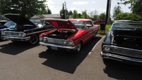 1964 Ford Fairlane - Three classic cars are parked in a lot, two with hoods open, under a sunny sky.