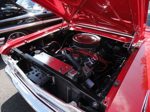 1964 Ford Fairlane - The engine bay of a red 1964 Ford Fairlane is open, revealing its V8 engine and chrome accents.