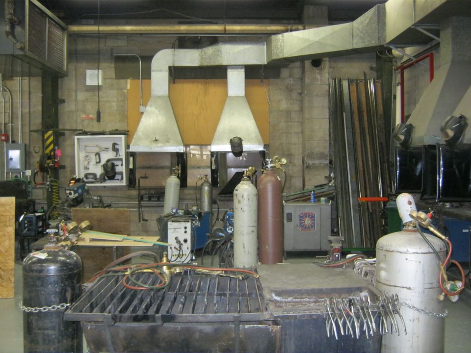 Welding shop interior with multiple gas cylinders, welding equipment, and metal stock