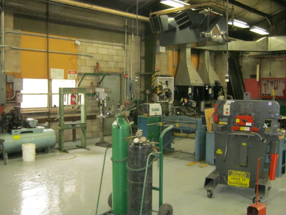 Workshop interior with air compressor, hydraulic press, welding equipment, and metal fabrication machinery