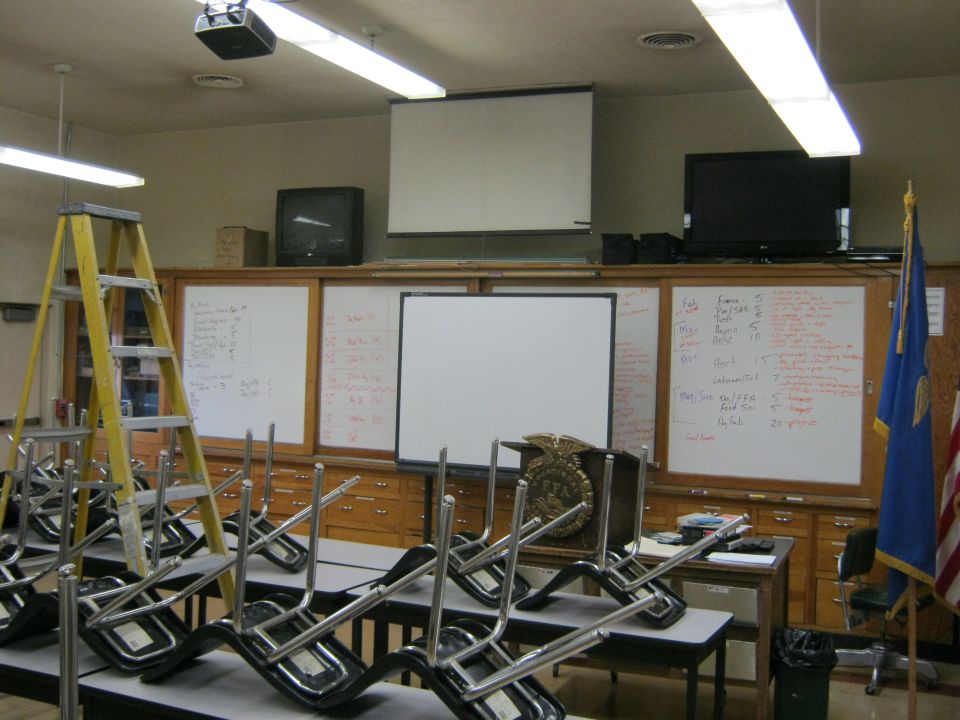 classroom with chairs stacked on tables, projector, screens, and whiteboards