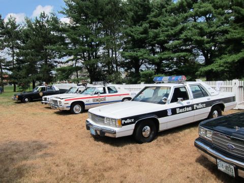 1991 Ford LTD Crown Victoria - lineup of classic police cruisers, including a black-and-white Boston Police sedan, displayed on grass at an outdoor show.