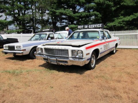 1991 Ford LTD Crown Victoria - Two 1970s full-size police sedans with red, white and blue striping and 'Not In Service' signs parked on a grassy field.