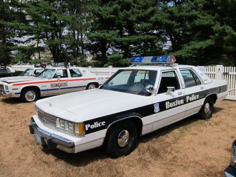 1991 Ford LTD Crown Victoria - black-and-white Boston Police Ford sedan with a roof light bar parked on grass beside other vintage cruisers.