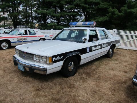 1991 Ford LTD Crown Victoria - black-and-white Boston Police Ford sedan with a blue light bar displayed on grass near a white fence and other cruisers.