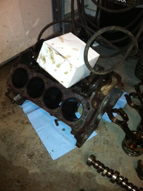 1991 Ford F-250 - Disassembled V8 engine block sitting on shop towels on a concrete floor, with a camshaft and connecting rods nearby.