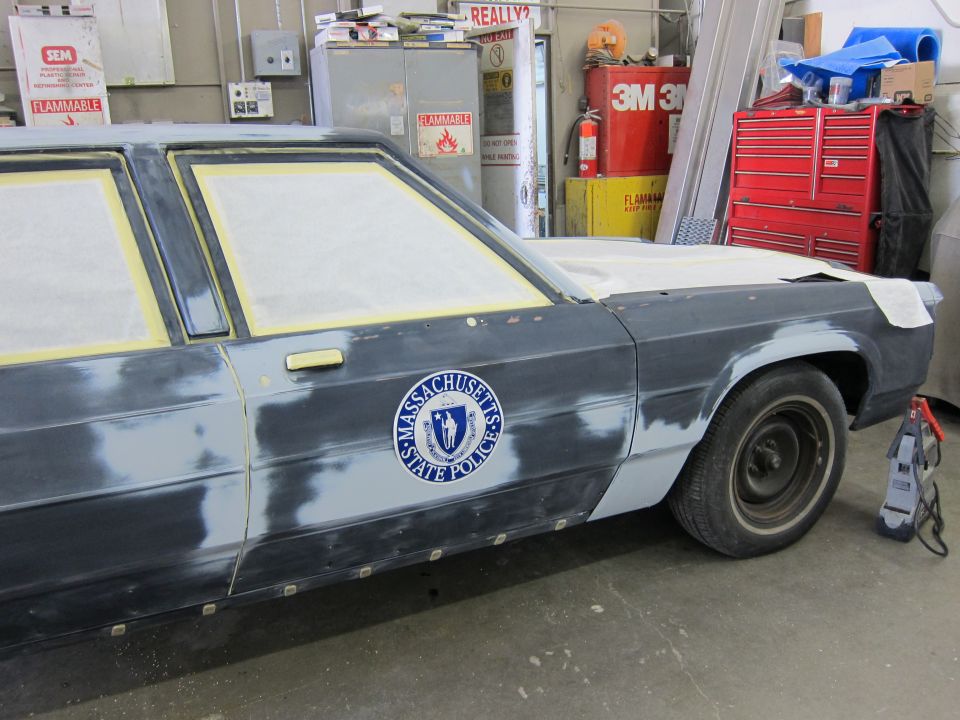 Side view of a dark sedan with Massachusetts State Police emblem, undergoing repairs