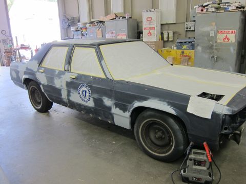 1991 Ford LTD Crown Victoria - Police car undergoing bodywork in a garage, with windows taped off and a circular badge visible on the door.