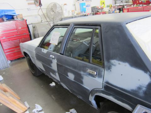 1991 Ford LTD Crown Victoria - A sedan is in a workshop, covered in primer and body filler, indicating it is undergoing repairs or customization.
