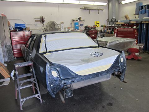 1991 Ford LTD Crown Victoria - A dark sedan is covered with protective sheeting in a workshop, likely undergoing repairs or preparation for painting.
