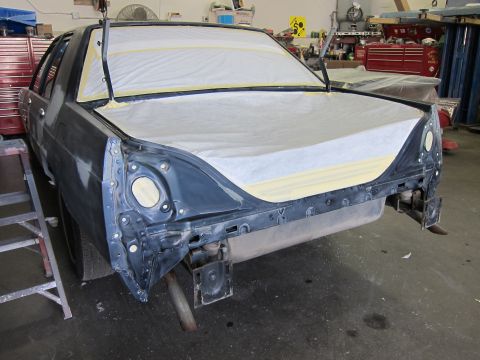 1991 Ford LTD Crown Victoria - A car's rear end is prepped for paint in a workshop, with the hood and trunk covered.