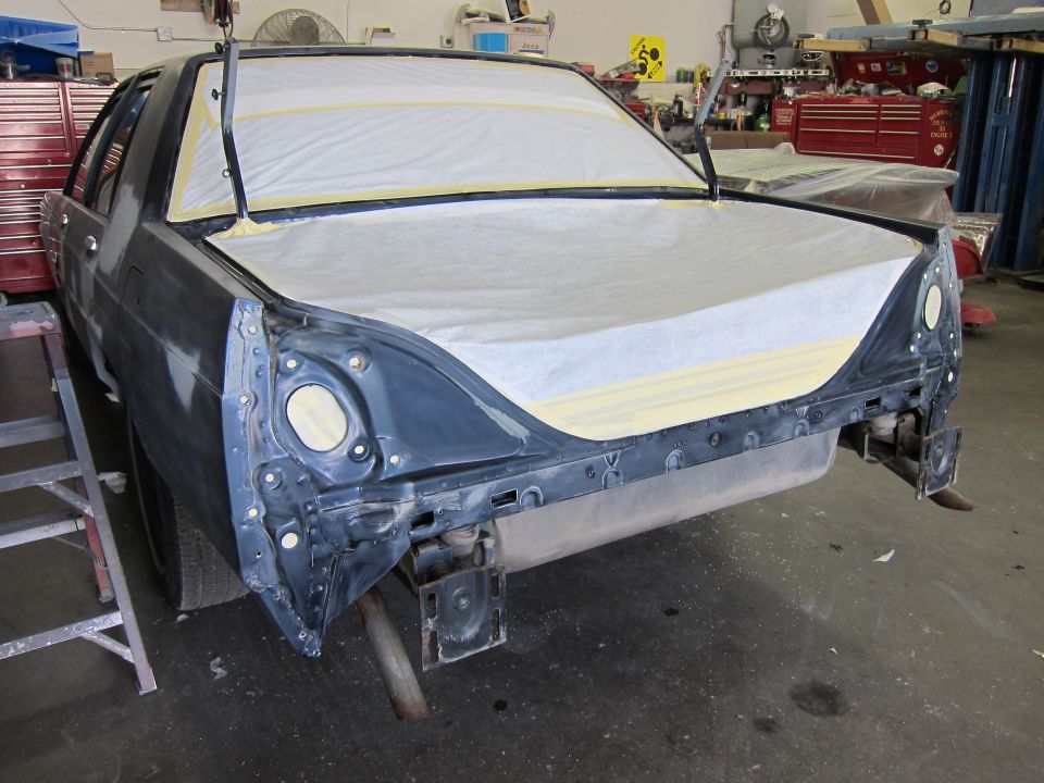 car body with hood and trunk covered in masking paper, in a workshop