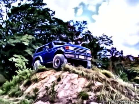 1992 Ford Bronco - A blue SUV navigates a steep, rocky incline under a cloudy sky.
