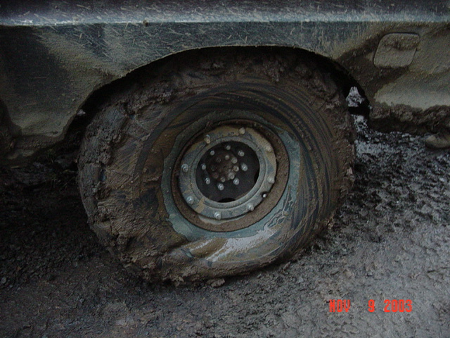 Close-up of a mud-packed off-road wheel and tire on a vehicle, lug nuts and rim caked in clay